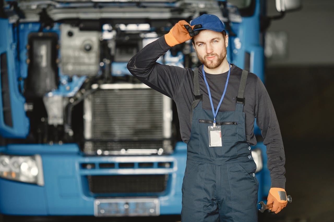Auto mechanic in uniform poses confidently with truck in background.