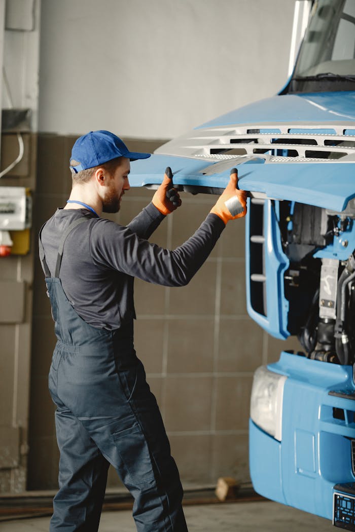 Mechanic in overalls fixing the front of a blue truck in a workshop garage.