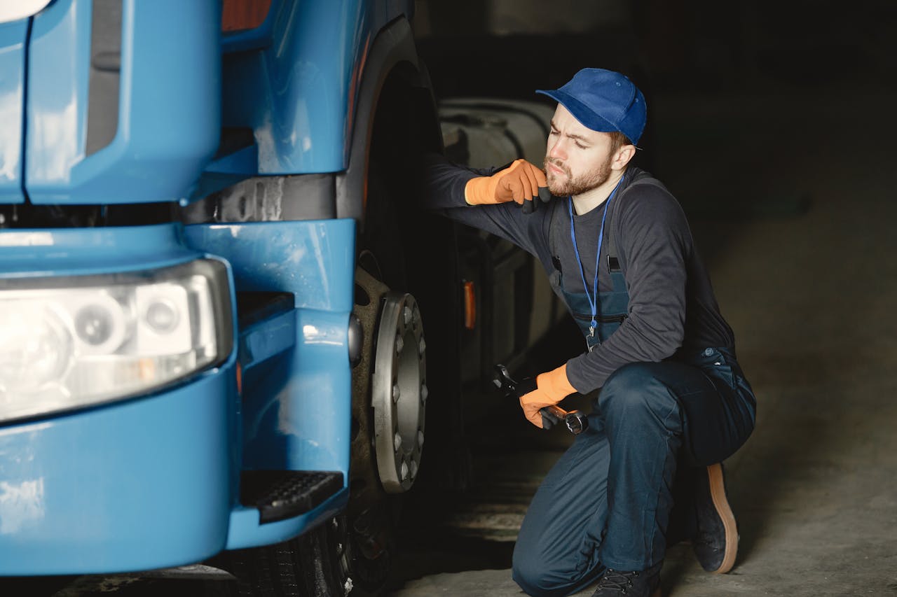 Pensive mechanic examining a truck wheel for maintenance in an indoor garage setting.